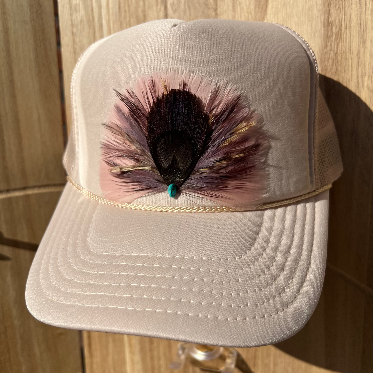 Beige cap with feather detail on a wooden surface