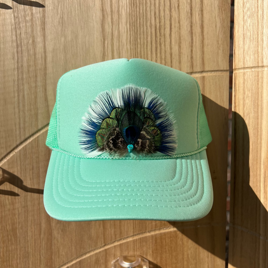 Mint green cap with peacock feather design on a wooden surface