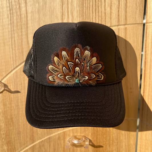 Black trucker cap with a decorative pheasant feather design on a wooden surface
