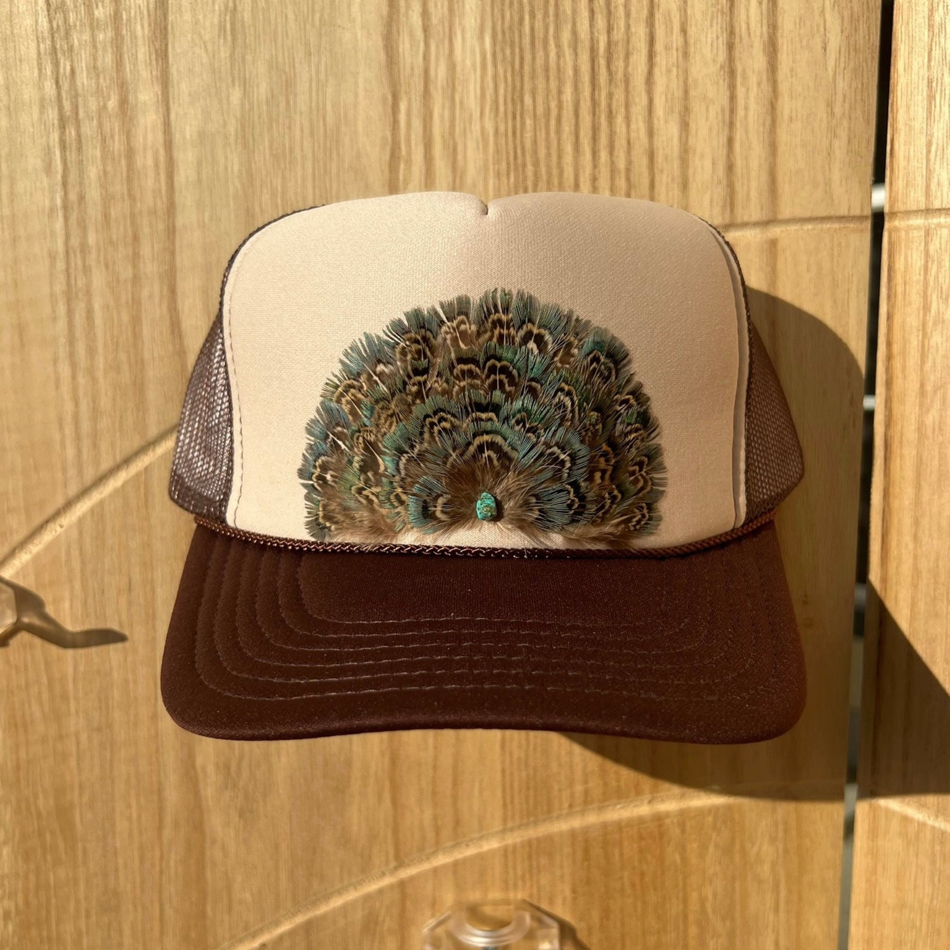 Trucker hat with peacock feather design on a wooden surface