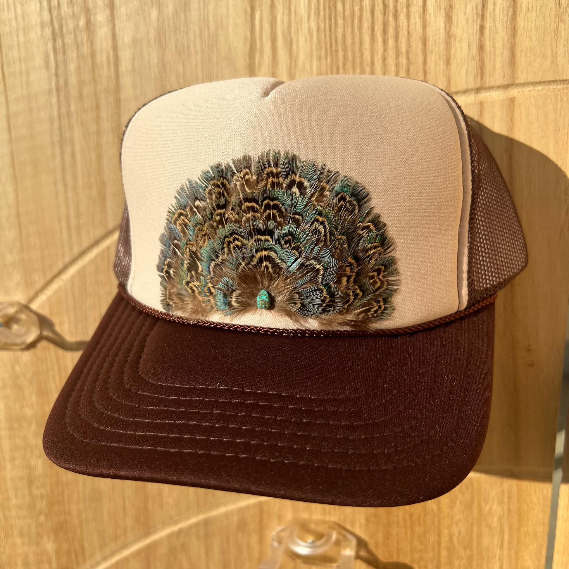 Trucker hat with peacock feather design on a wooden surface