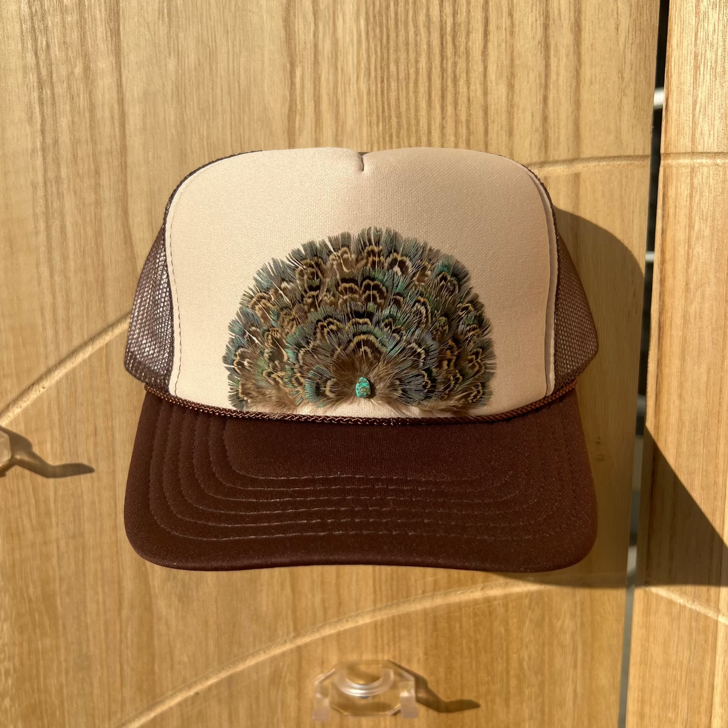 Trucker hat with peacock feather design on a wooden surface