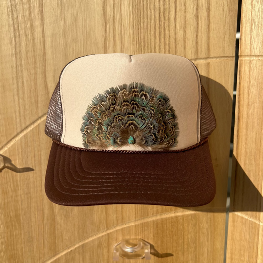 Trucker hat with peacock feather design on a wooden surface