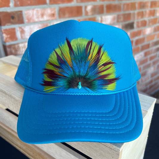 Blue cap with colorful feather design on a wooden surface with a brick wall background