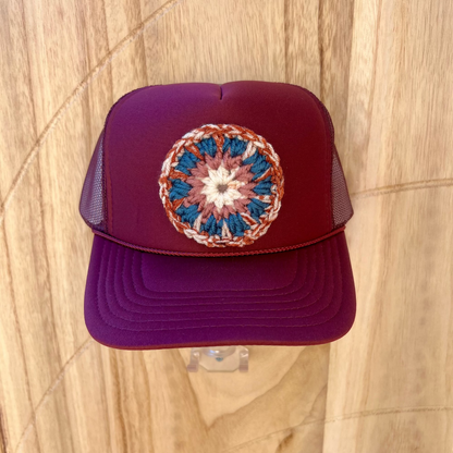 Maroon trucker cap with a colorful circular crochet design on a wooden surface