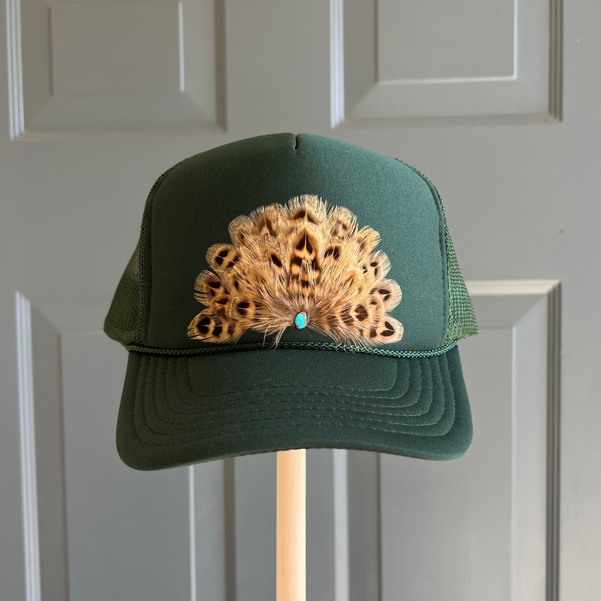 Front view of Volant Style trucker hat in hunter green featuring hand-placed tan brown feathers with a center turquoise stone.