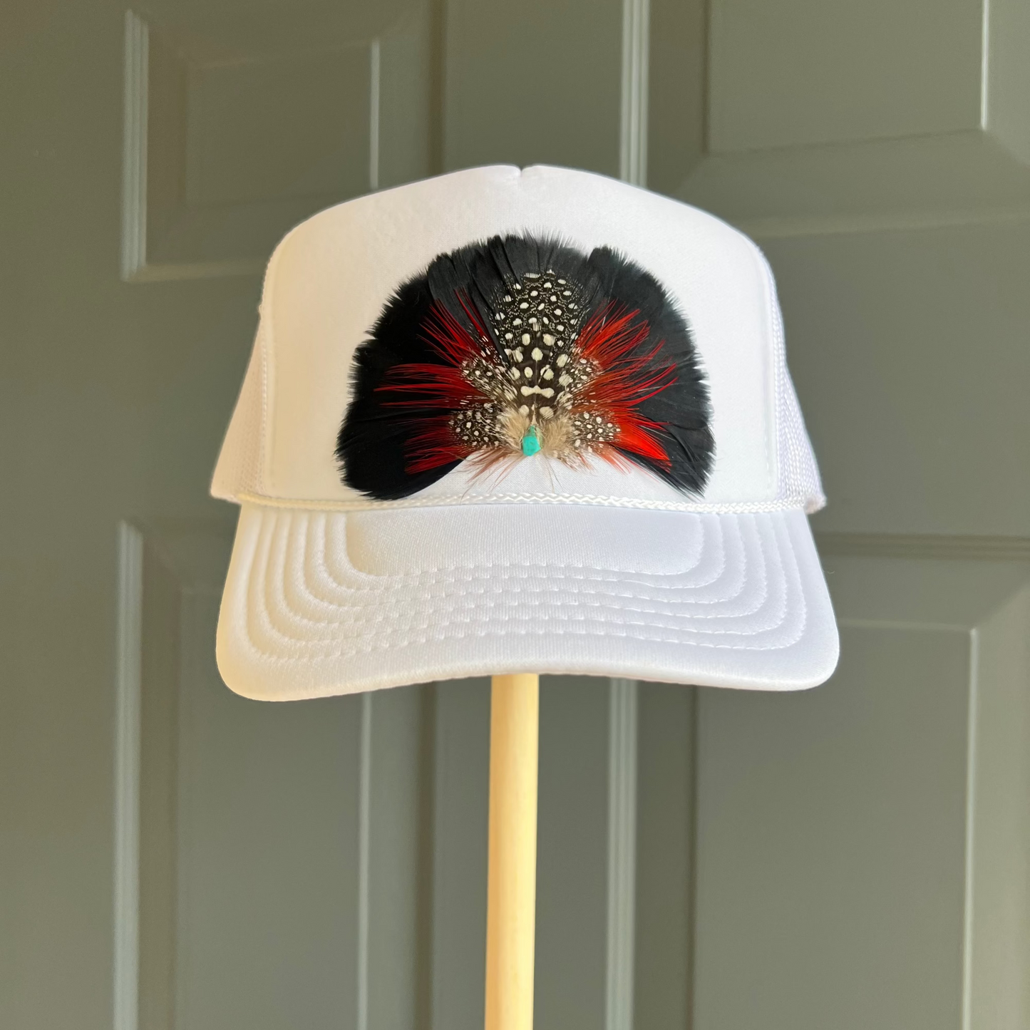 White cap with feather design on a stand against a green door background
