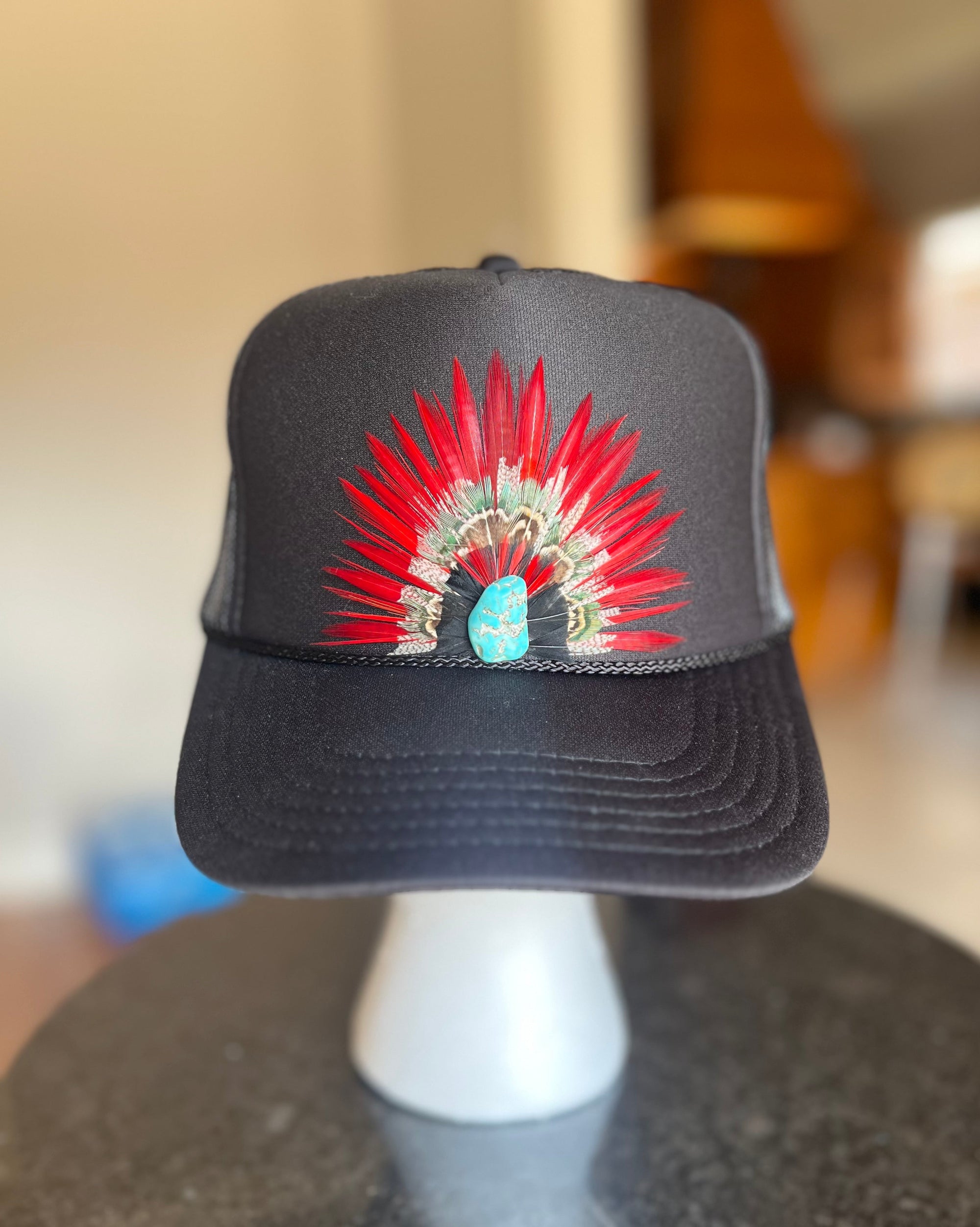 Black cap with a colorful headdress design on a mannequin head against a blurred indoor background.