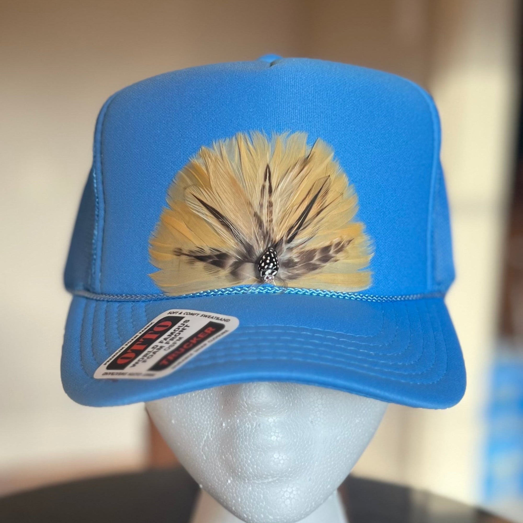 Blue cap with feather design on a mannequin head against a neutral background