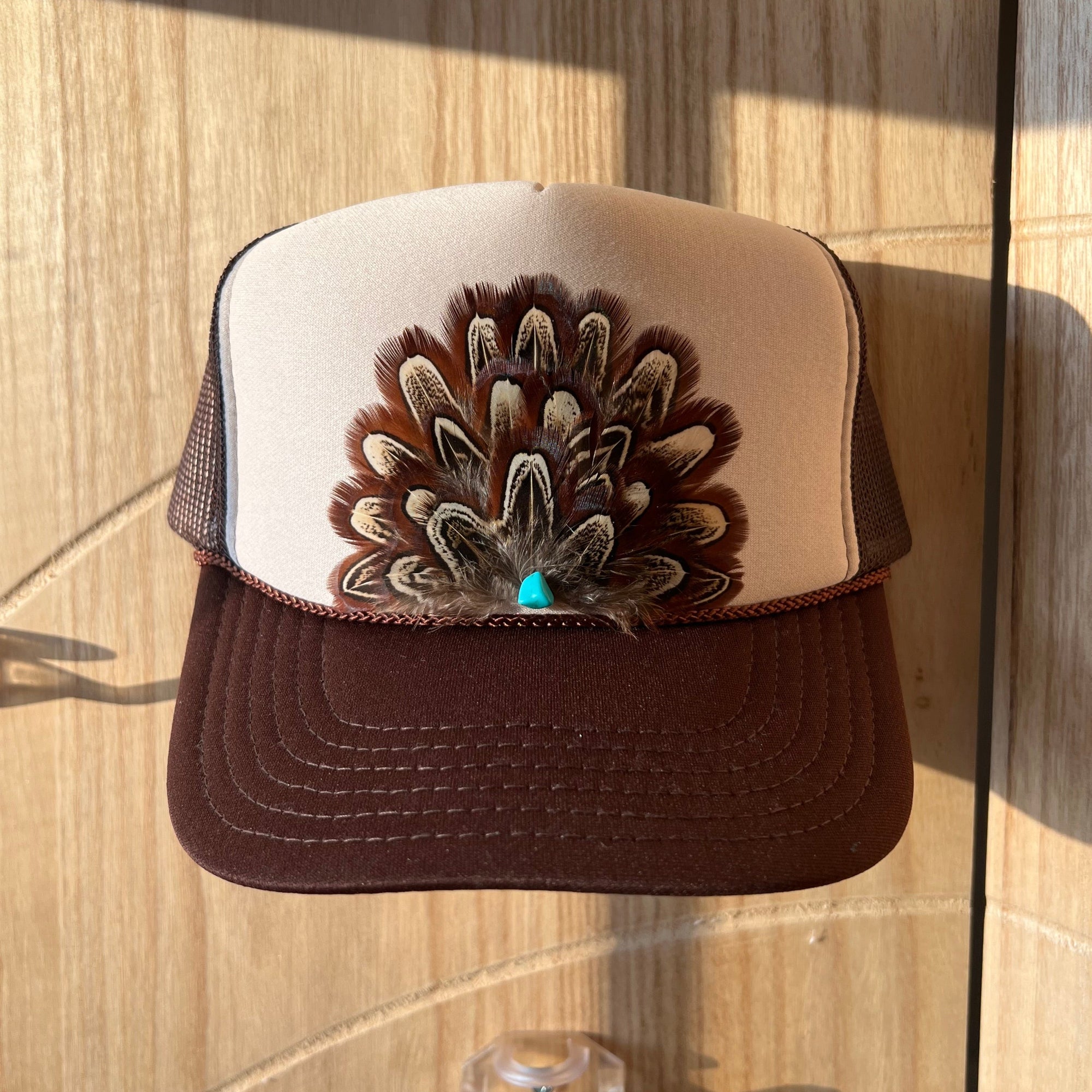 Brown and beige cap with a decorative feather design on a wooden surface