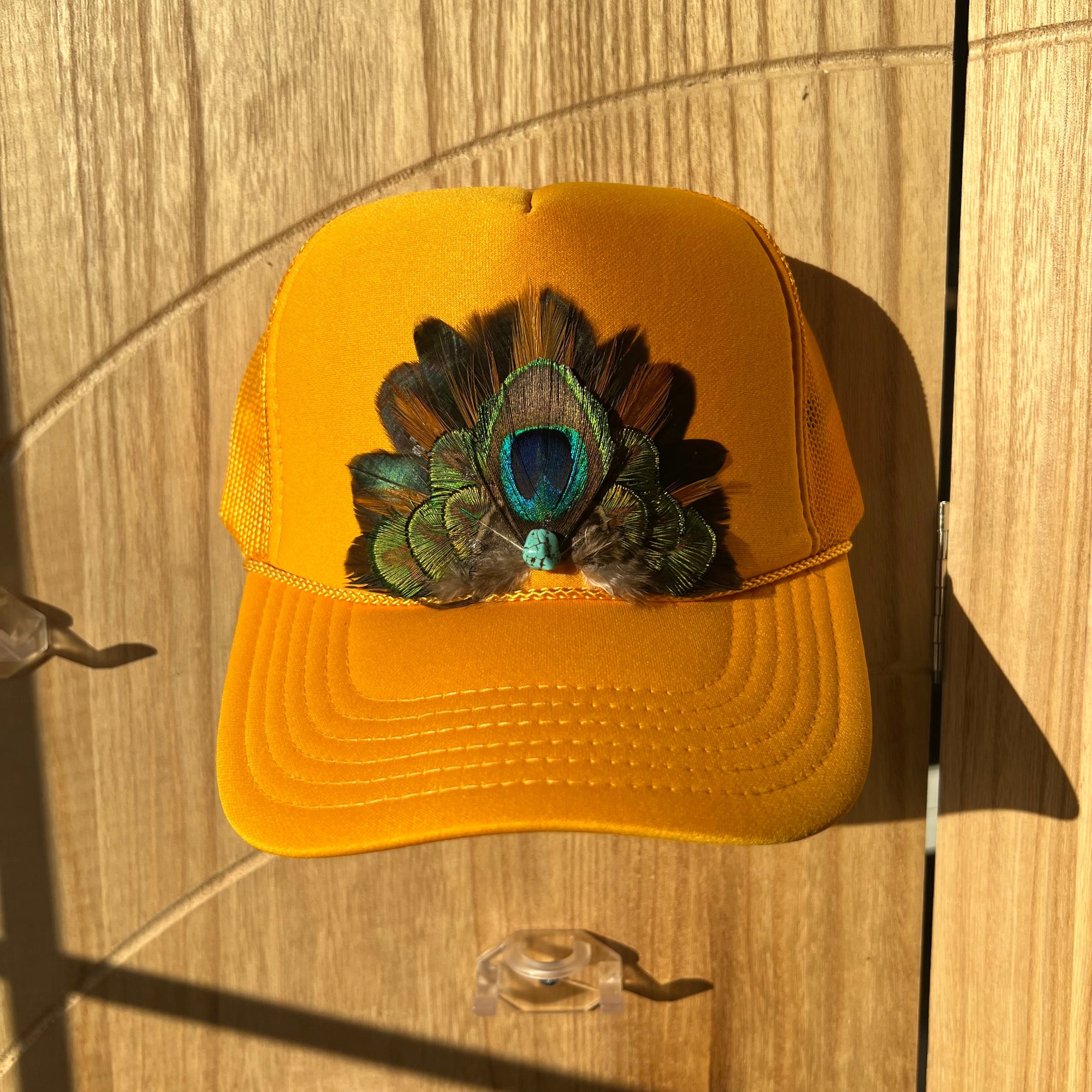 Yellow cap with peacock feather design on a wooden surface