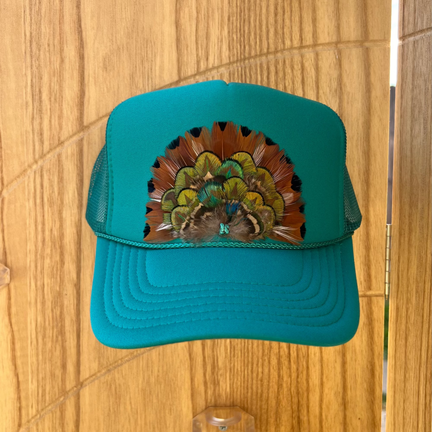Teal cap with a feather design on a wooden surface