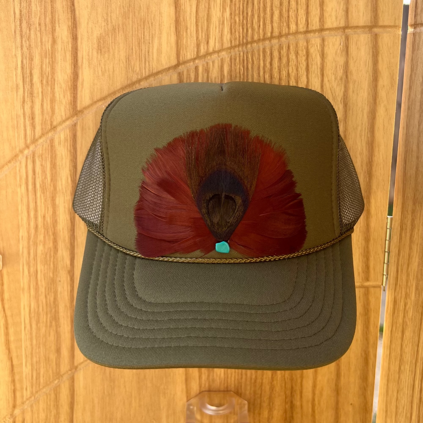 Green cap with a red feather with peacock design on a wooden surface