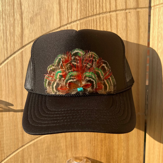 Black trucker cap with colorful feathers on a wooden surface