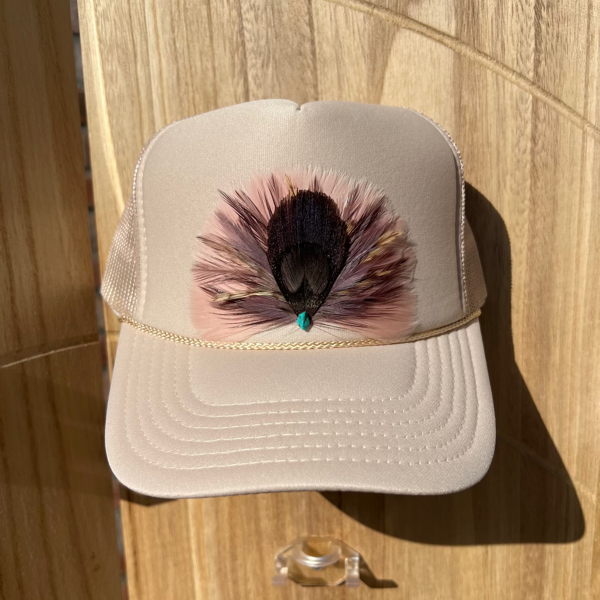 Beige cap with peacock feather design on a wooden surface